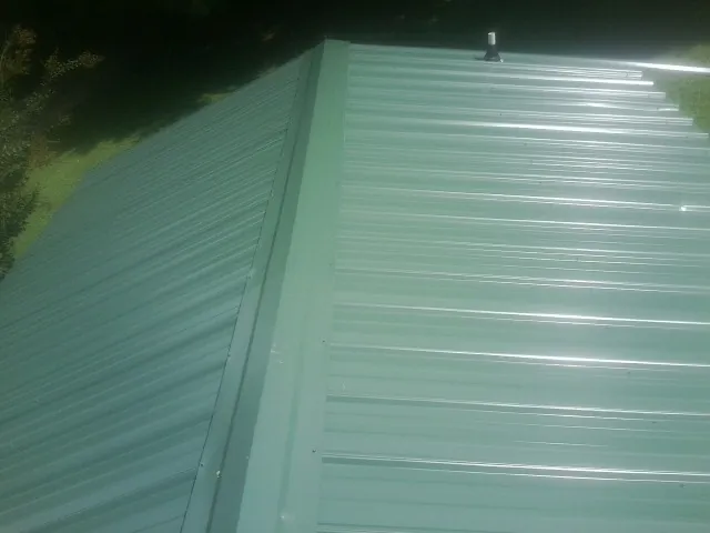 New green metal panels meeting at the ridge of a roof — Flat Roof Repair work by our crew in Toledo