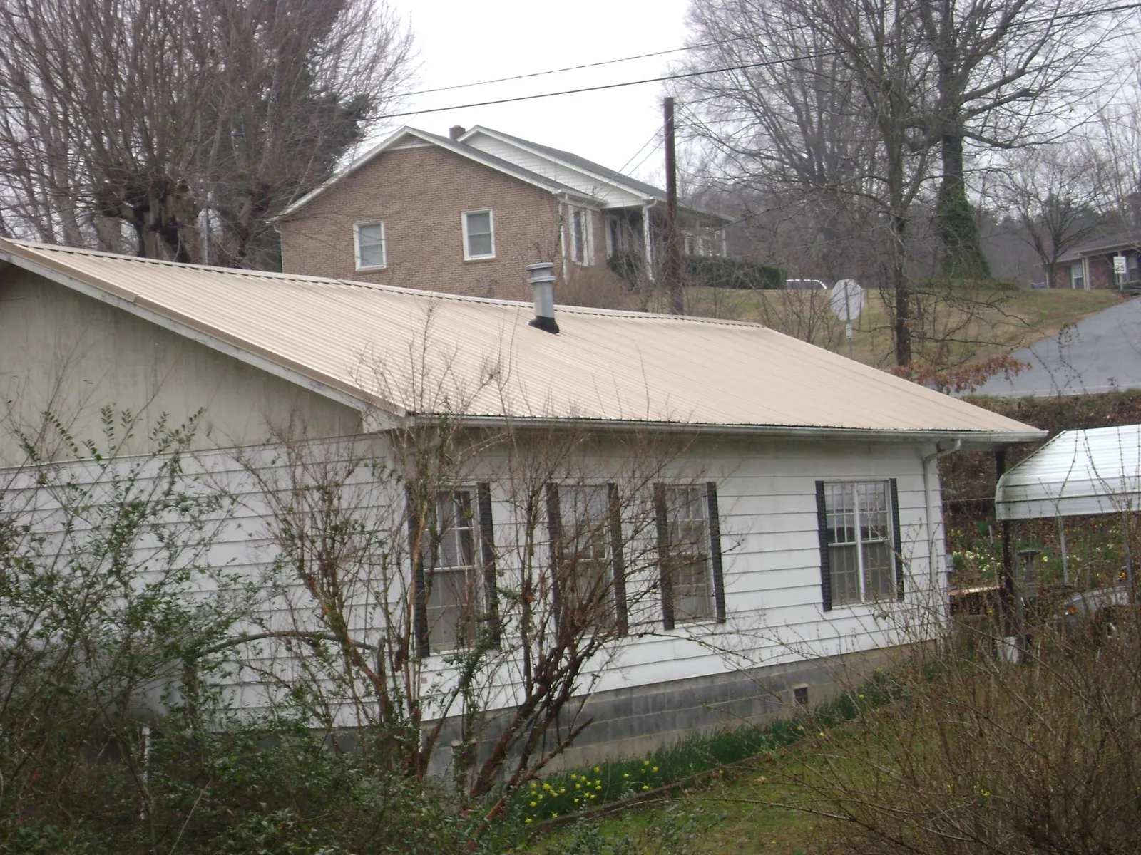 Tan metal roof on a white sided house set into a hillside — Commercial Roofing by Roofing Brothers in Toledo